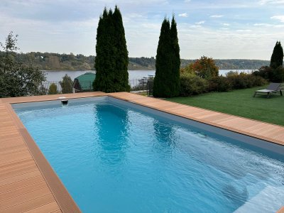 Прямоугольный бассейн с голубой водой на светло-коричневой террасе среди растительности