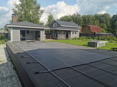 Композитный бассейн с темным защитным покрытием на деревянном настиле рядом со строениями